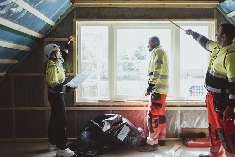 Female building contractor examining window with male construction worker at site