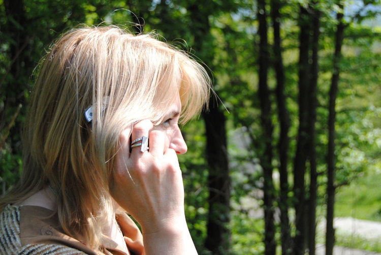 Close-up side view of woman with blond hair answering mobile phone in park