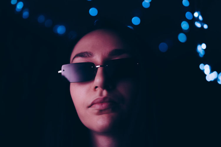 Portrait of confident young woman wearing sunglasses at illuminated restaurant