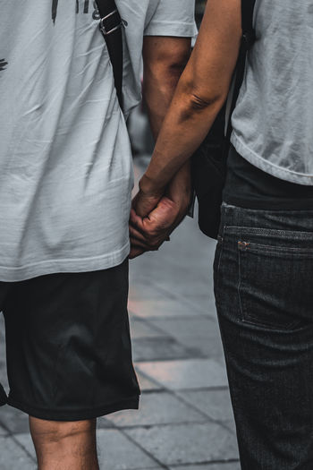 Midsection of gay couple holding hands while standing on street