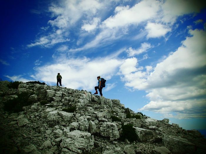 People climbing on rock against sky