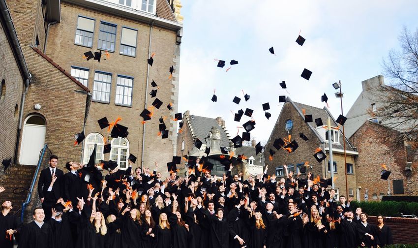 Students throwing mortarboards in air against sky