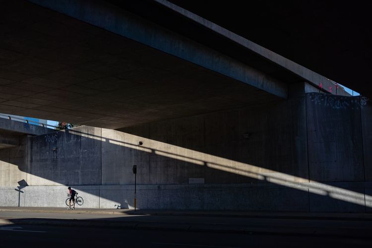 Man with bicycle walking under bridge in city