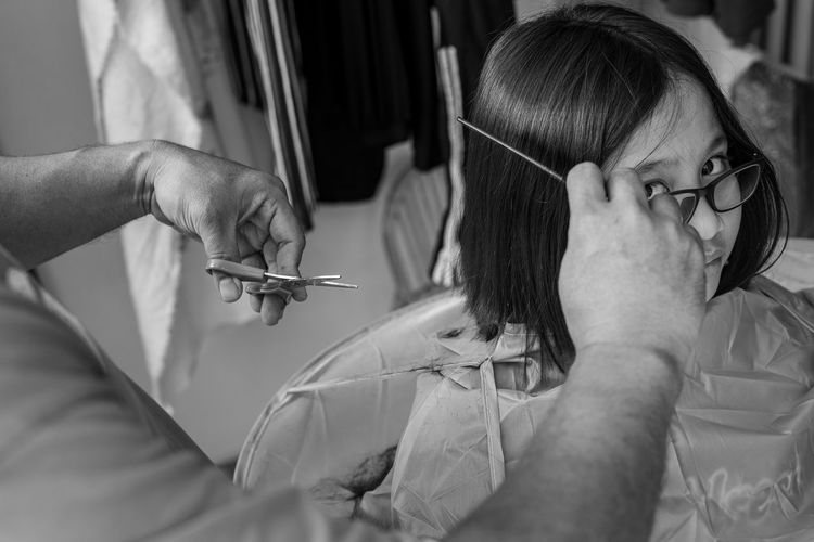 A girl getting haircut at home from the father. monochrome, black and white.