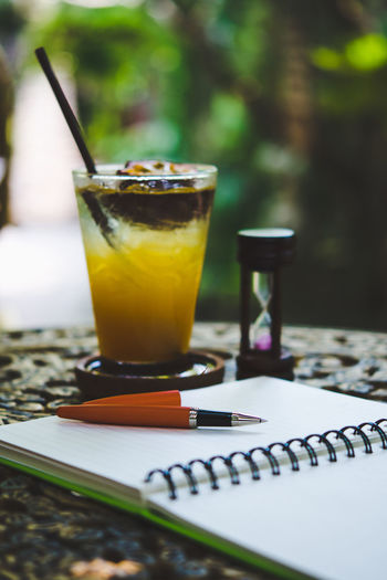 Fresh passion fruit juice in glass on table with is tree garden background, notepad and pen