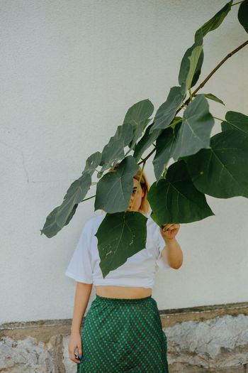 Woman holding leaves while standing against wall