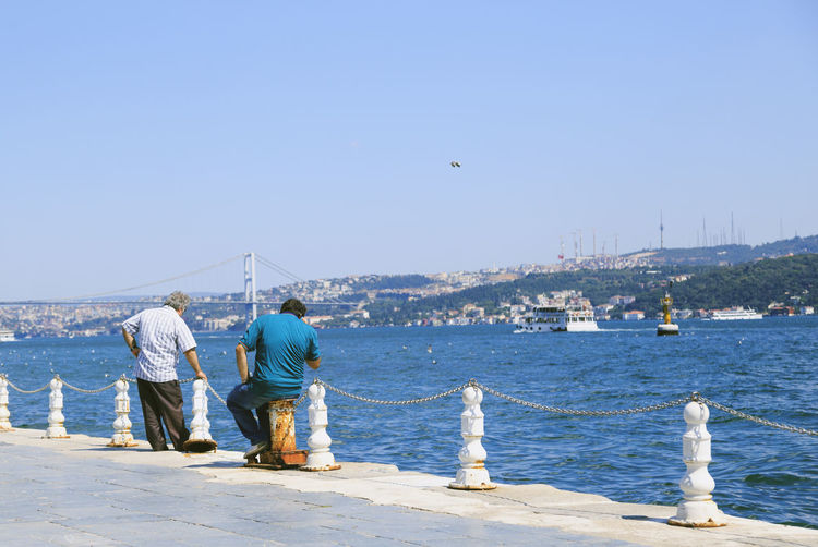 Rear view of men on pier over river against clear sky