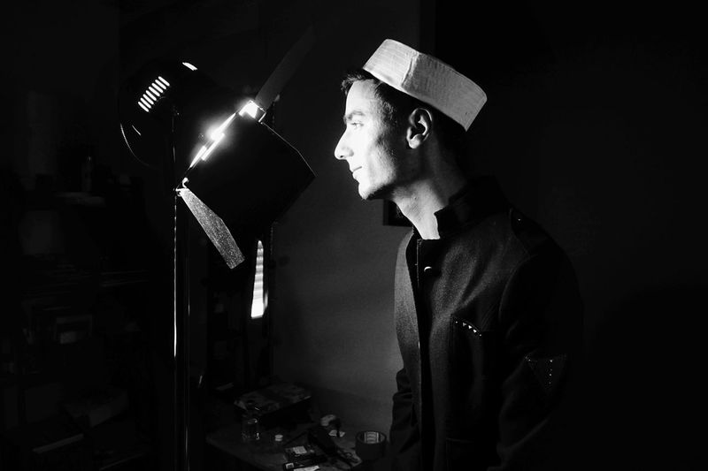 Side view of young man standing in front of illuminated stage light at studio