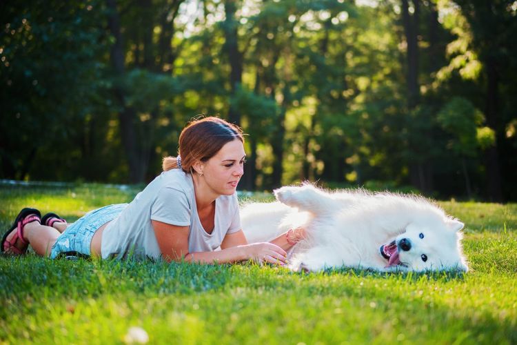 Woman lying with dog on grassy field at back yard