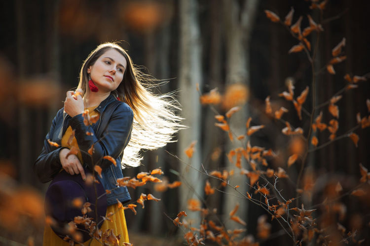 Thoughtful woman tossing hair while standing in forest during autumn