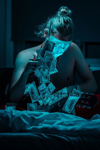 Young man wearing mask while sitting with money and guitar on bed