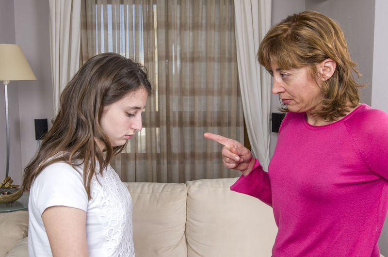 Mother scolding daughter while standing in living room at home