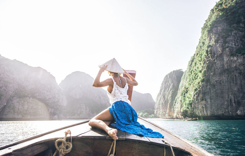 Man sitting on boat against sea and mountains against sky