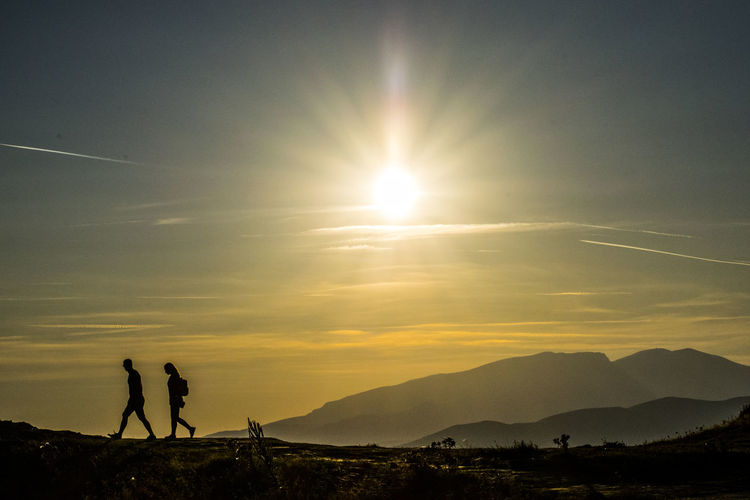 Silhouette people walking on mountain against sky during sunset