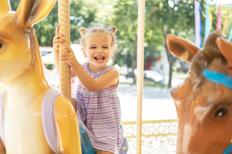 Funny little kid girl in colorful dress rides on carousel in an amusement park in summer day