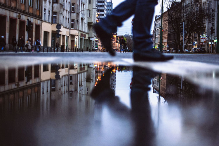 Low section of man walking by puddle in city at dusk