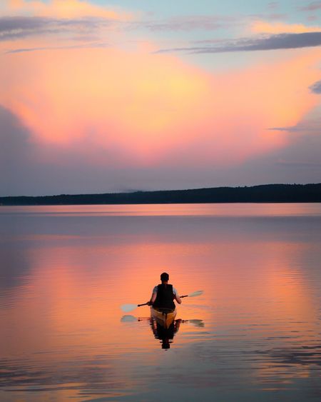Rear view of man canoeing on sea against sky during sunset