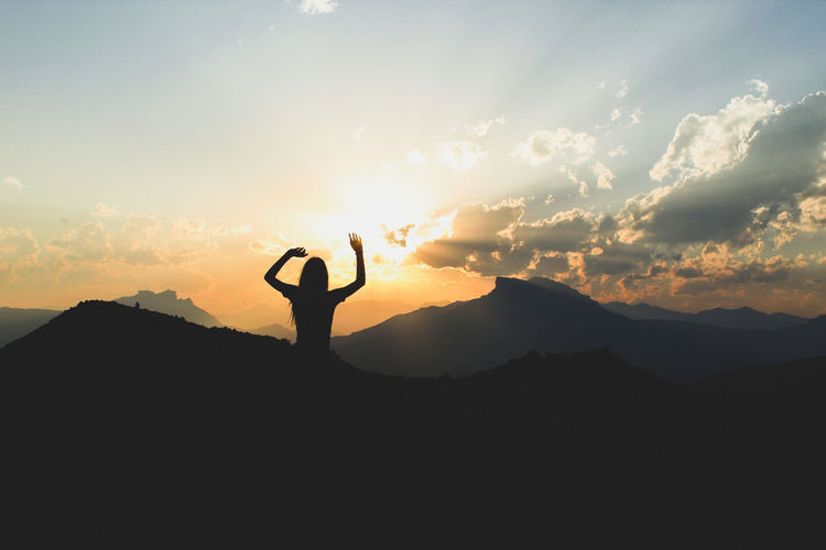 Silhouette woman with arms raised standing on mountain against at sunrise