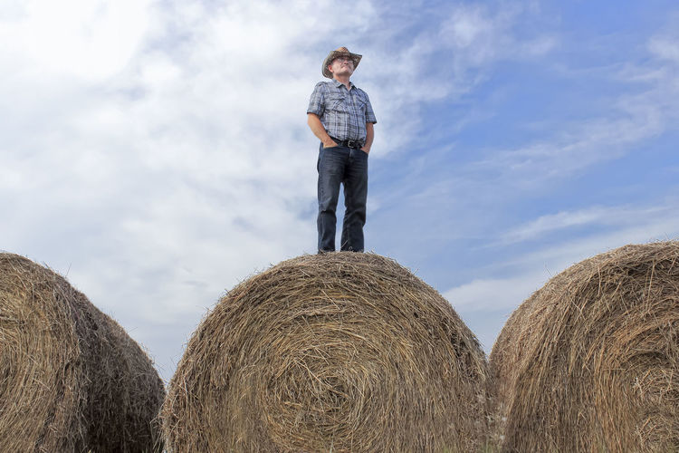 Man standing by hay bales on field against sky