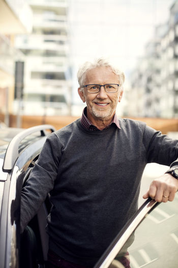 Portrait of smiling senior man disembarking from car in city