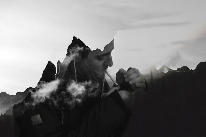 Digital composite image of man smoking cigarette with mountains against sky