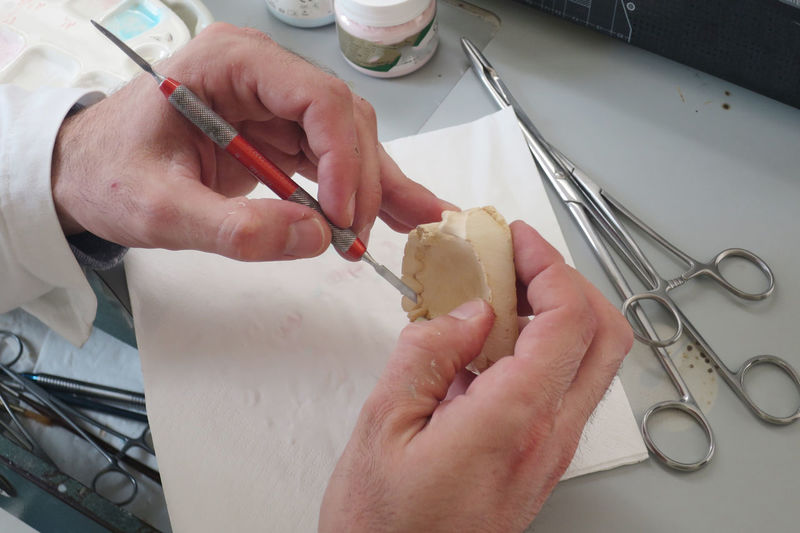 Cropped hands of male dentist making dentures mold at desk