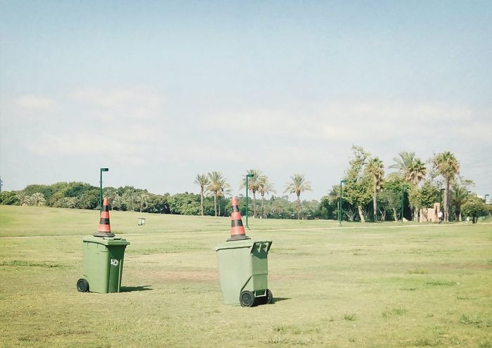 Garbage cans with traffic cones on grassy field against sky