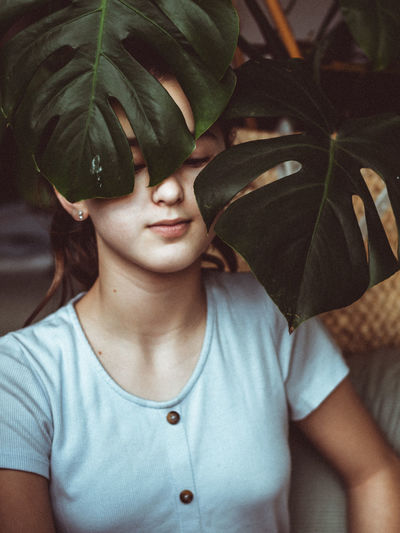 Young girl playing with monstera at home.
