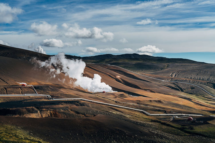 Smoke emitting from dramatic landscape against sky