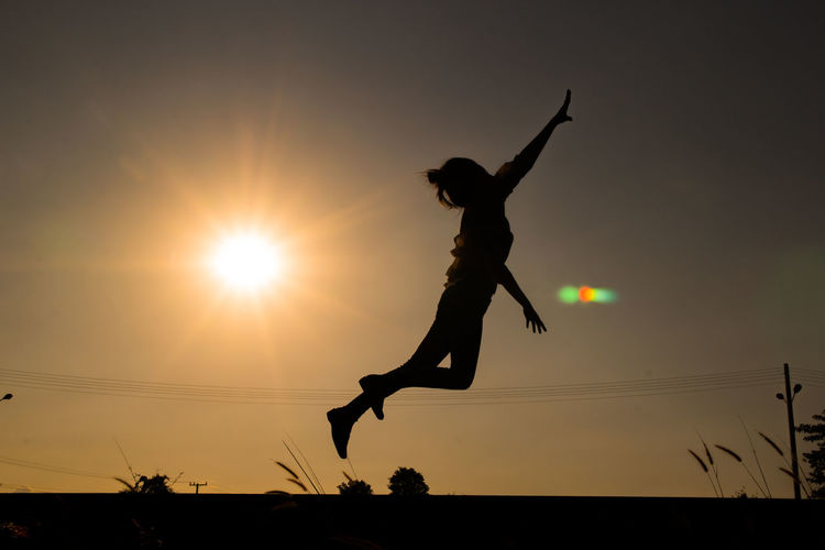 Side view of silhouette woman jumping against sky during sunset
