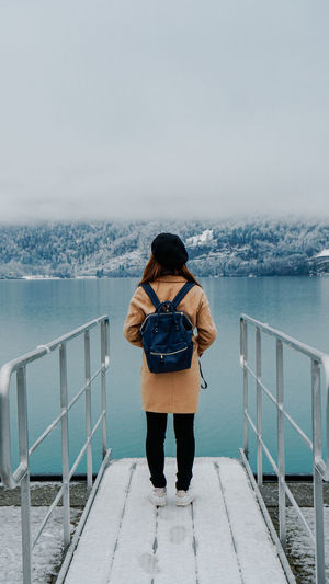 Rear view of backpack woman standing by lake during winter