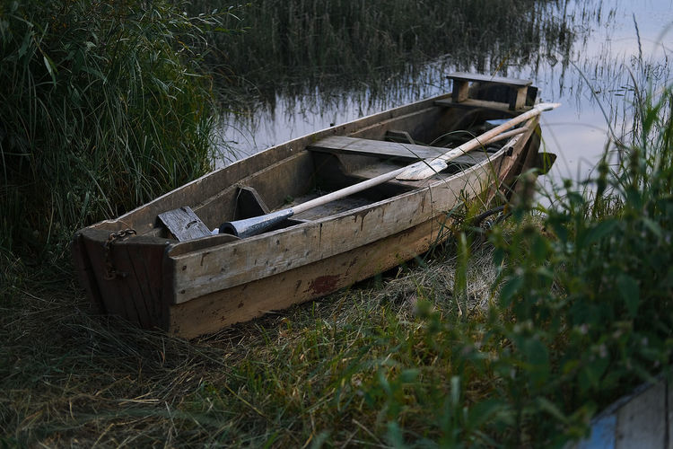 Abandoned boat moored on field by lake