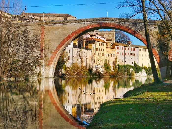 Arch bridge over lake by buildings against sky