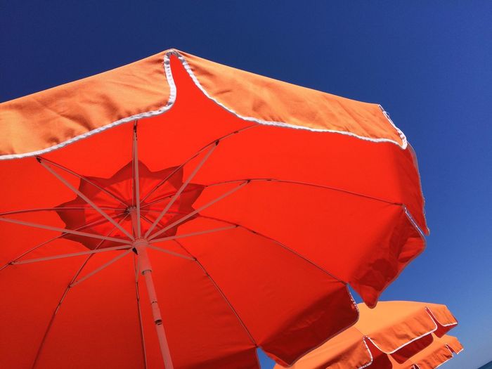 Low angle view of red umbrella against clear blue sky