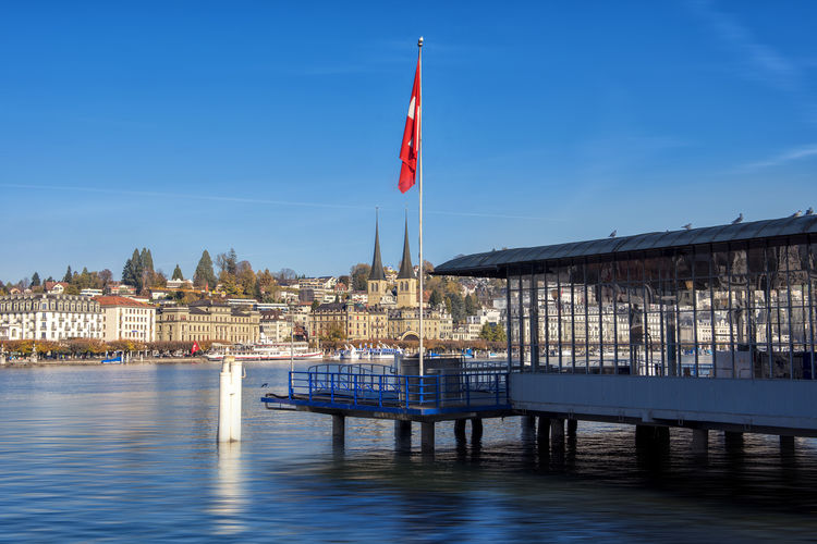 Swiss flag on pier in lake against blue sky