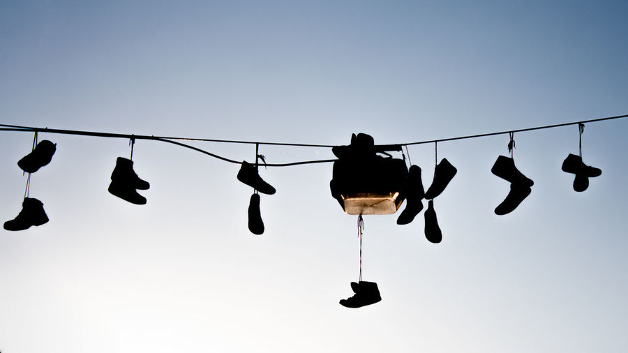 Low angle view of silhouette shoes hanging on cable against clear sky at sunset