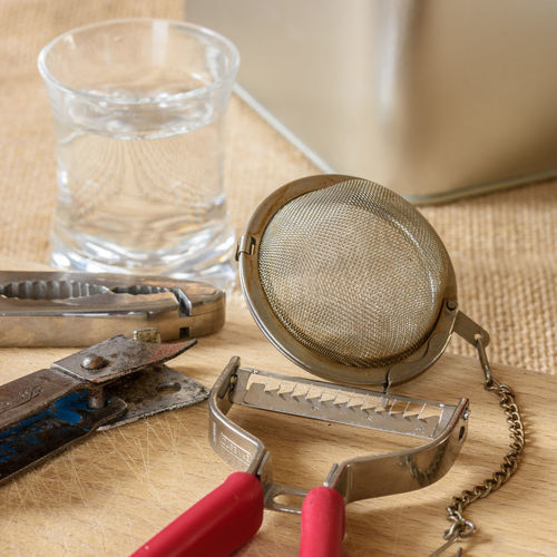 High angle view of peeler and tea strainer with water glass on wooden table