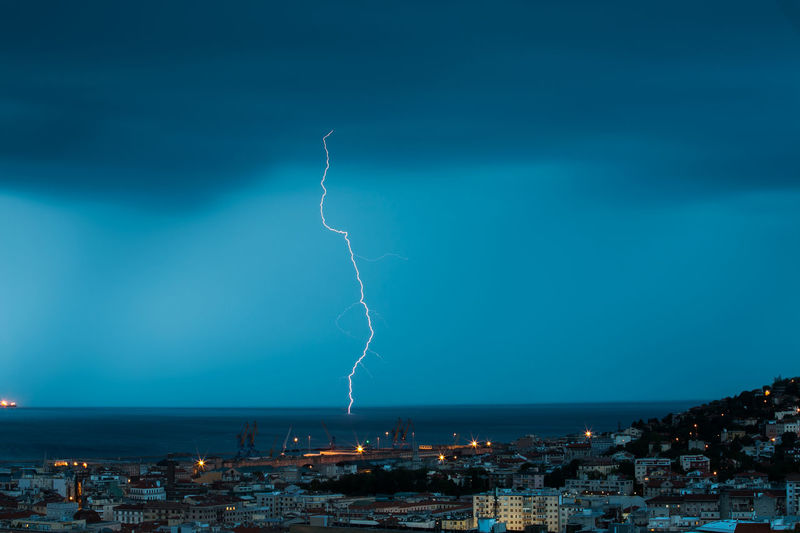 Lightning over sea by city at dusk