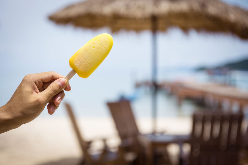 Cropped hand holding ice pop at beach