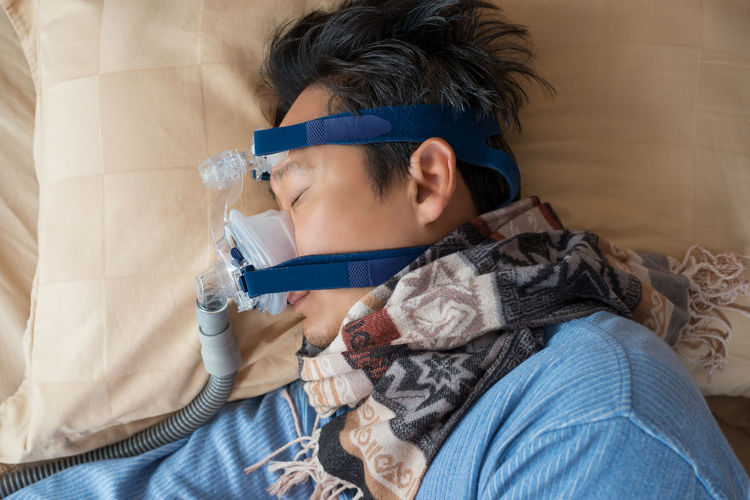 High angle view of mature man wearing oxygen mask while sleeping on bed