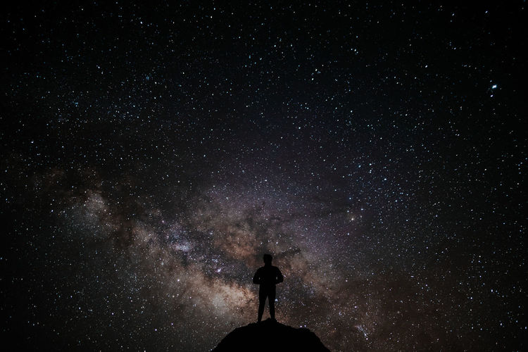 Silhouette man standing on cliff against star field at night