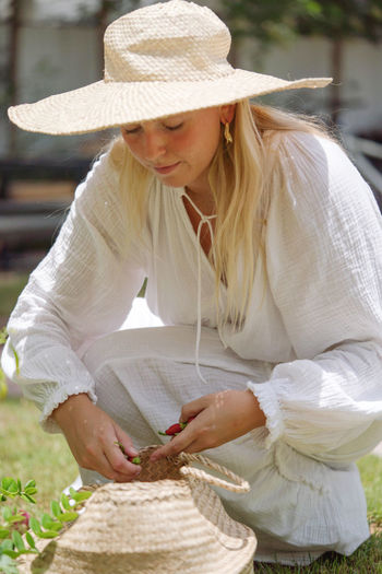 Woman wearing straw hat and a white dress picking red chilies in the garden