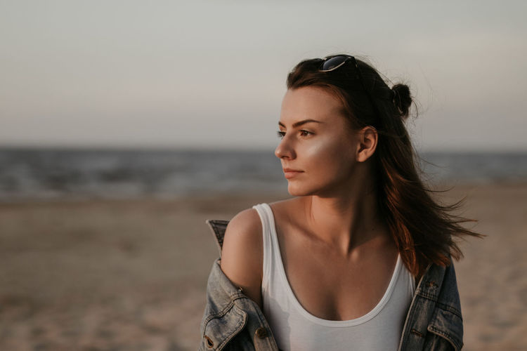 Portrait of beautiful woman standing at beach against sky