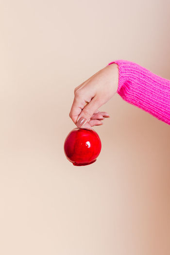 Close-up of hand holding apple against pink background