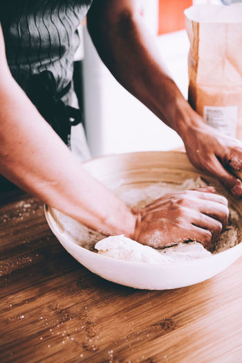 Midsection of man kneading dough in bowl at table