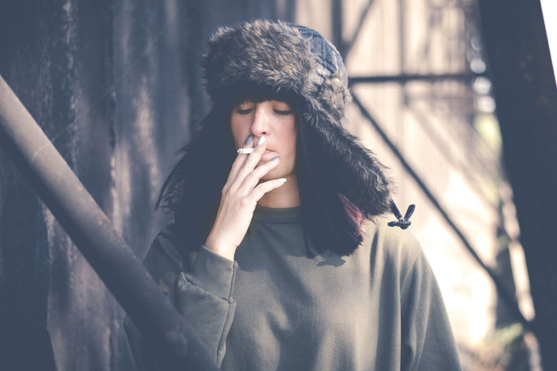 Close-up of young woman smoking cigarette by wall