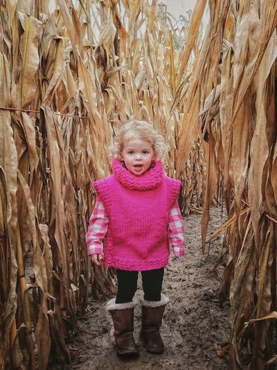 Portrait of cute baby girl standing amidst plants in farm
