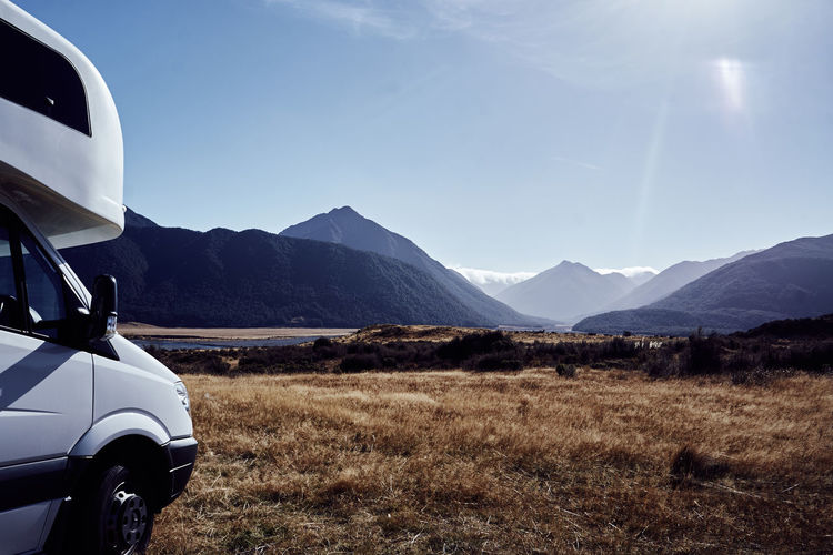 Cropped image of travel trailer on grassy field by mountains against clear sky