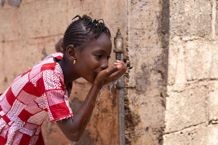 Girl drinking water from faucet against wall