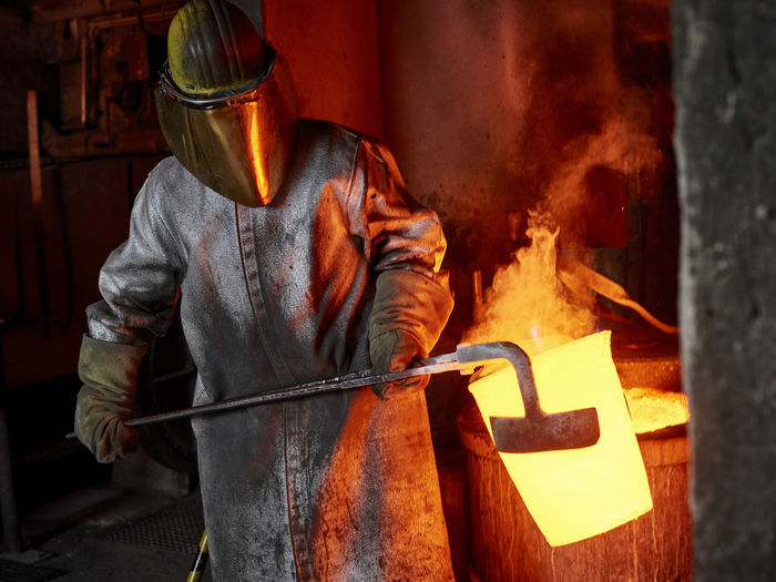 Foundry worker carrying burning container with hand tool in industry